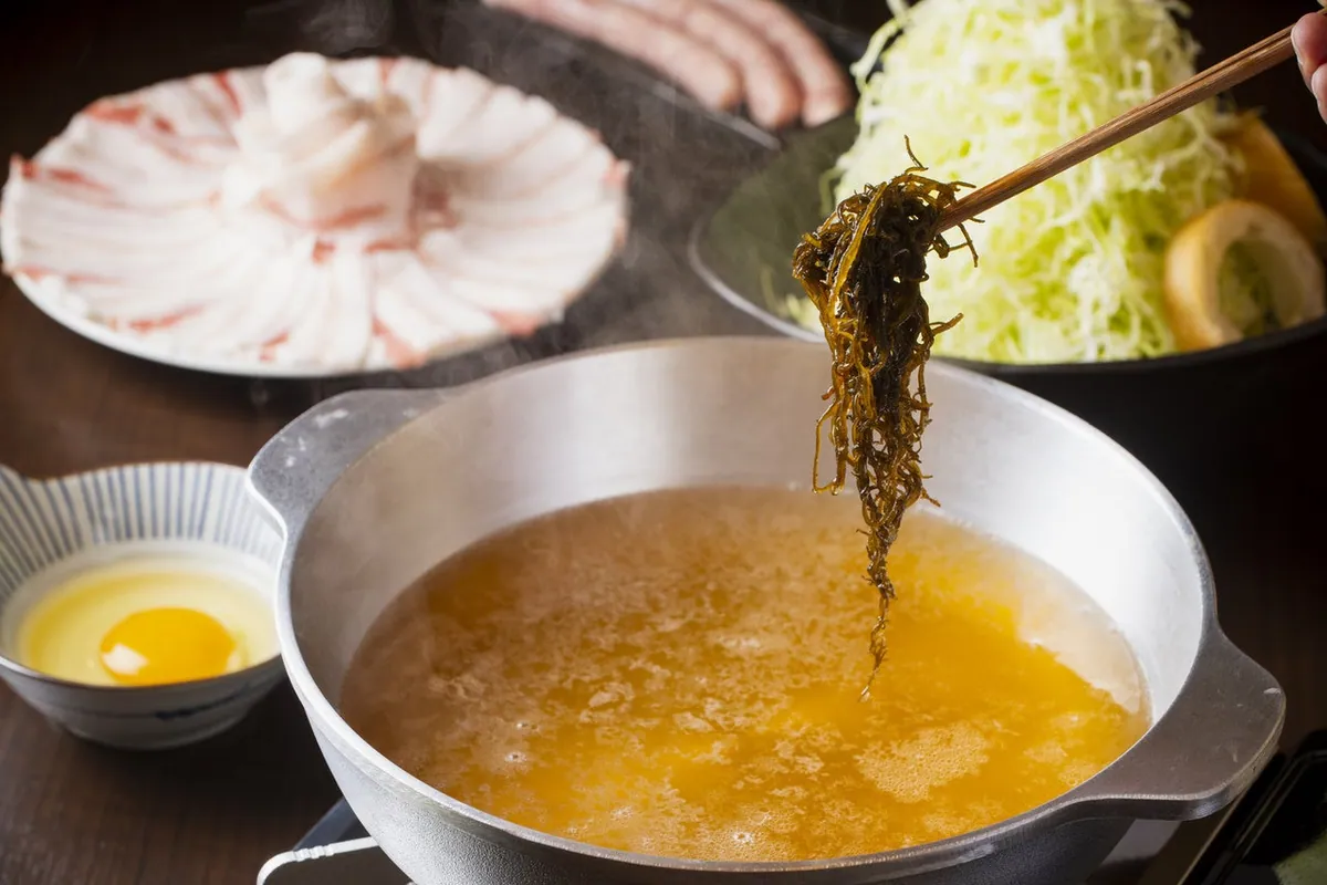 しゃぶしゃぶ鍋にもずくを入れる箸と、豚肉・キャベツ・卵