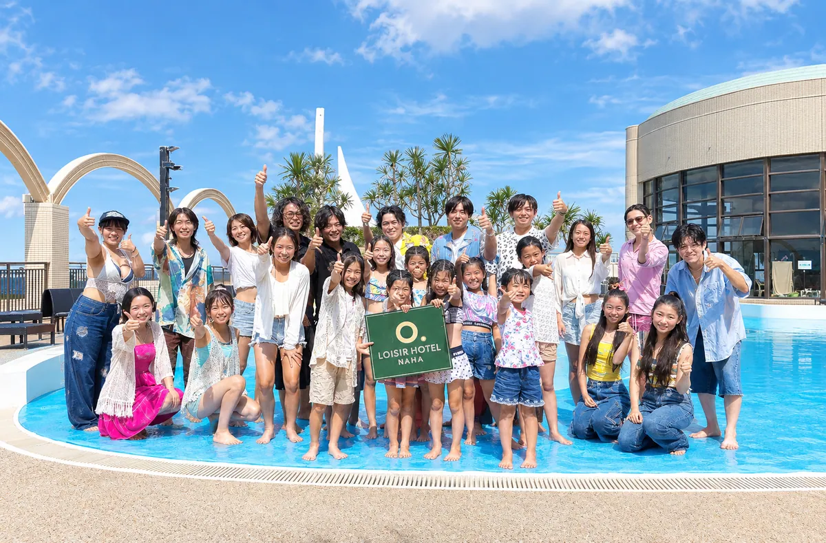 プールサイドでエキストラの人たちと並ぶ撮影の集合写真